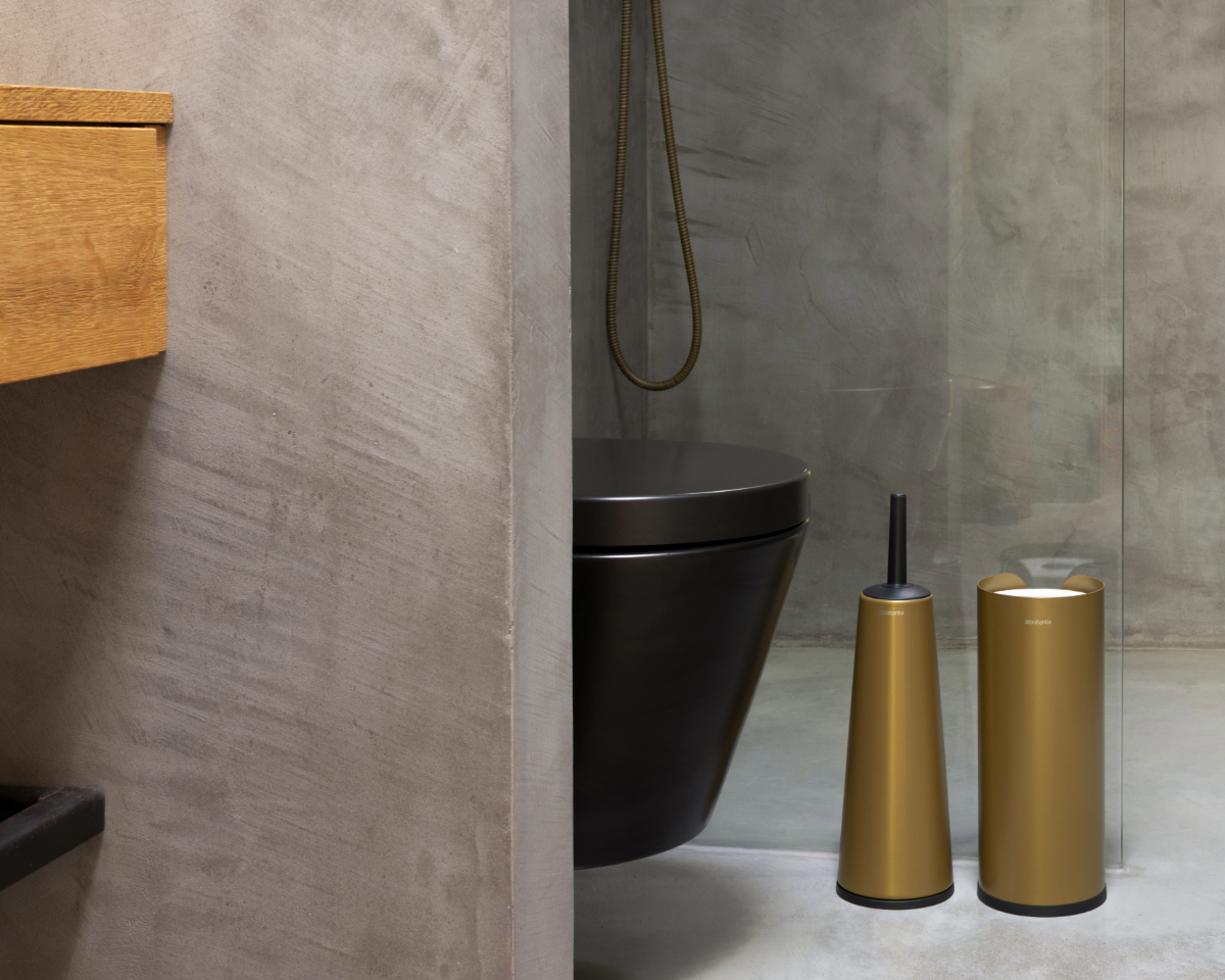 Warme Metallfarben für den NewIcon Pedal Bin 5L und verschiedene ReNew Produkte in Warm Gold Ein grauer Raum mit einer Toilette und ReNew Produkten in Warm Gold, die dem Raum eine warme Atmosphäre verleihen