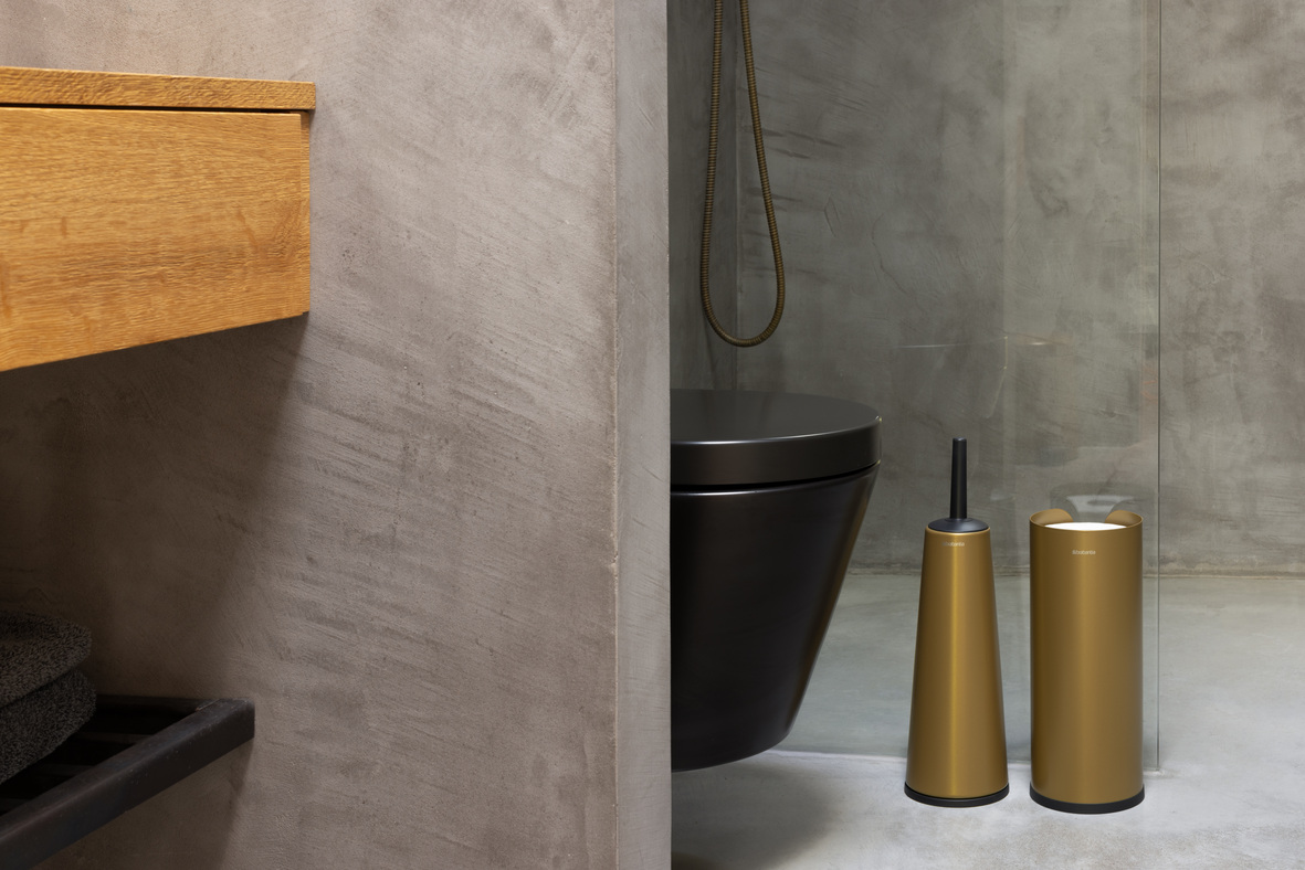 Een grijze kamer met een toilet en ReNew producten in Warm Gold, wat de ruimte een warme sfeer geeft